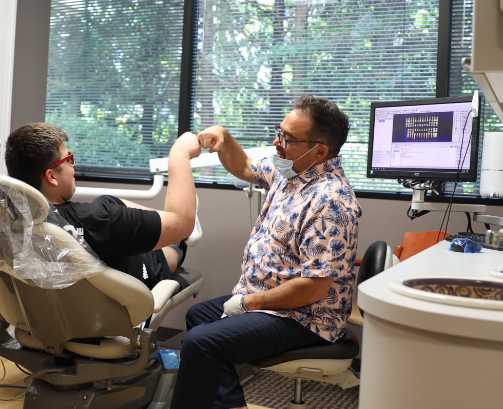 Doctor high-fiving young man sitting in dentist's chair